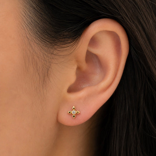 Close-up of an ear wearing a gold star-shaped earring with a central gemstone.