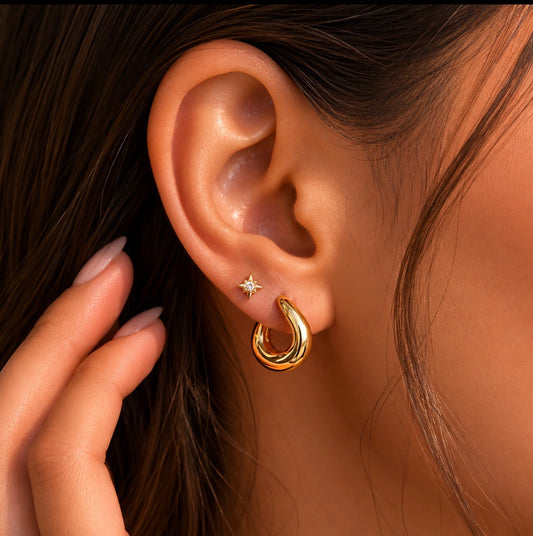 Close-up of an ear wearing a gold statement twisted hoop earring with a star stud in second piercing.