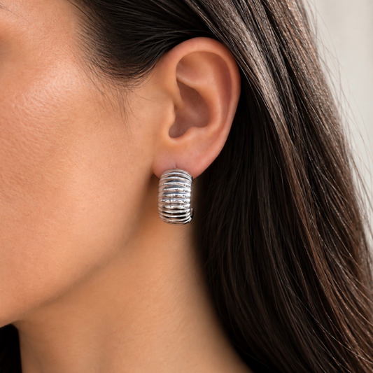 A close-up of a model's ear wearing a textured, ribbed silver hoop earring.