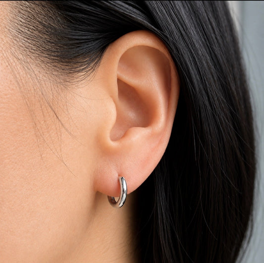 A close-up of a person's ear wearing a small polished silver hoop earring.