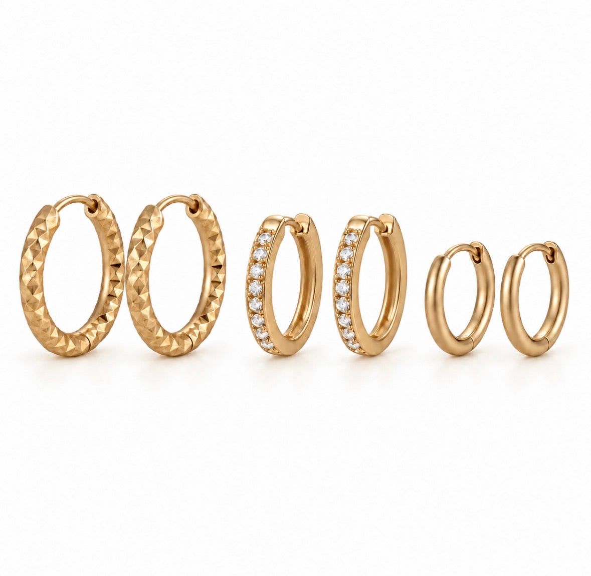 three pairs of gold huggie hoop earrings in different sizes, displayed on a clean white background. The earrings feature various textures and settings, including a textured diamond-cut finish, a pavé-set row of clear stones, and smooth polished finishes.