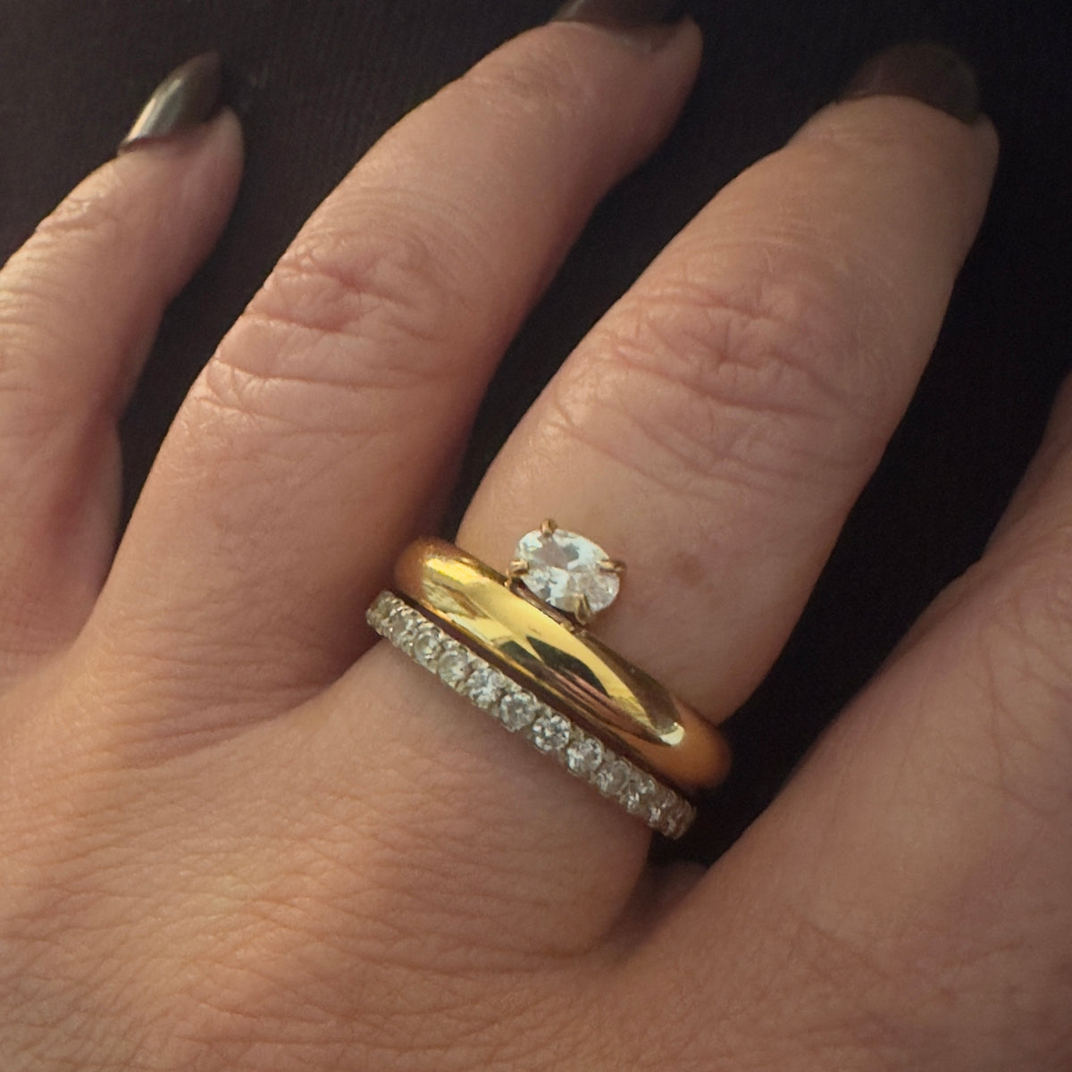 Close-up of a hand wearing two gold rings with diamond accents on a dark background