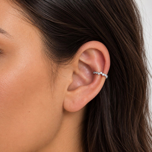 A close-up of a woman's ear wearing a delicate silver ear cuff adorned with small clear stones.