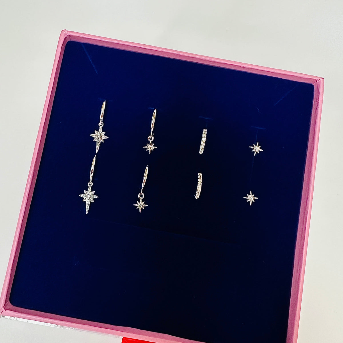 A set of five silver star and crescent moon drop earrings displayed inside a pink-lined dark blue jewelry box.