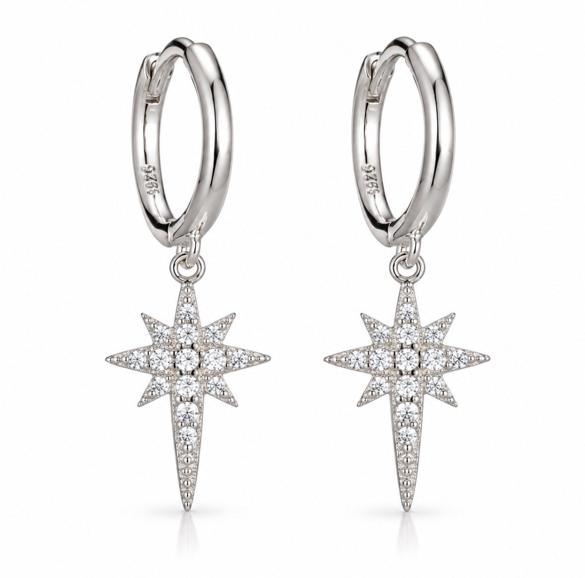 A pair of silver huggie hoop earrings with dangling starburst charms paved with clear stones, shown on a clean white background.