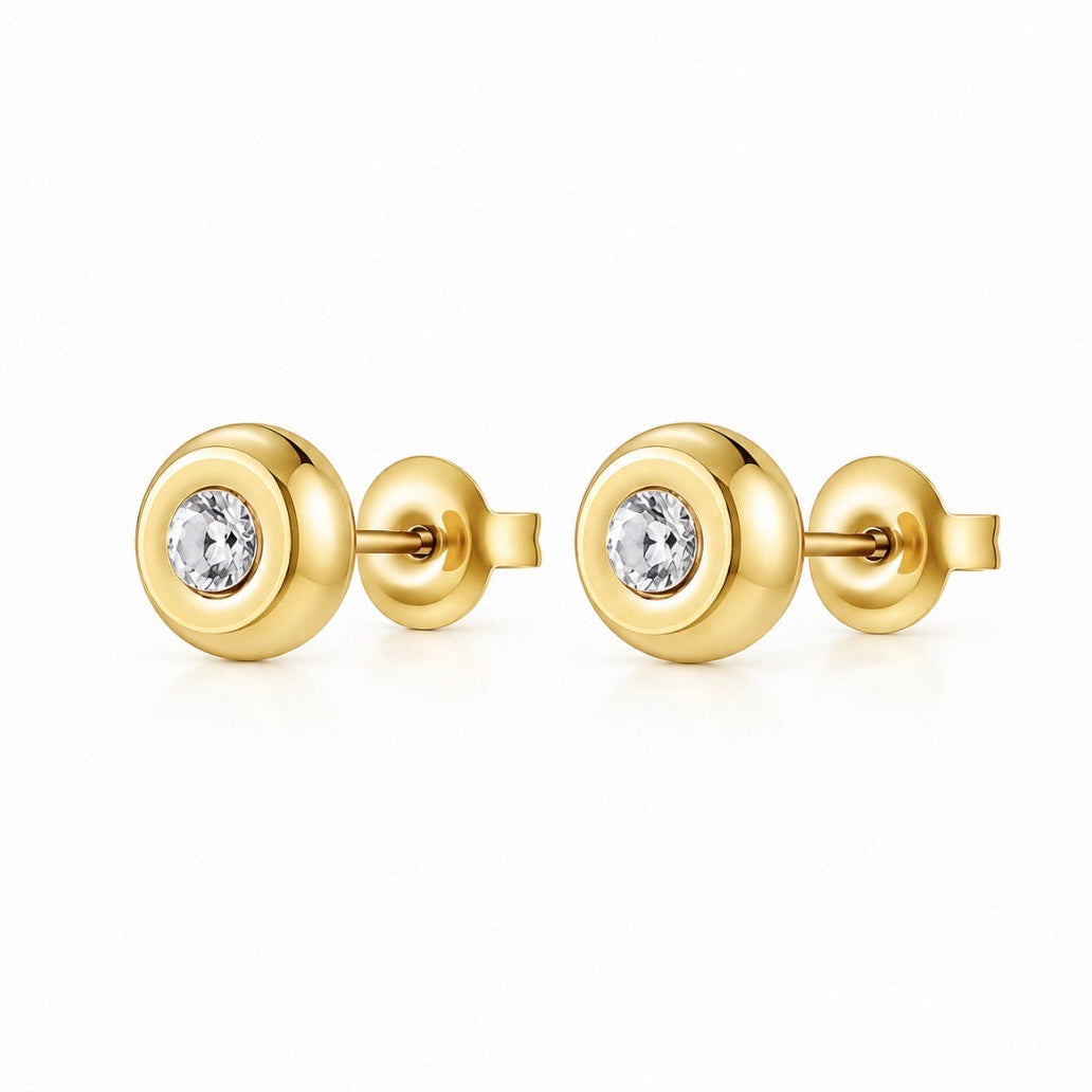 A pair of gold stud earrings with a circular bezel setting holding a clear round-cut gemstone, shown on a clean white background.