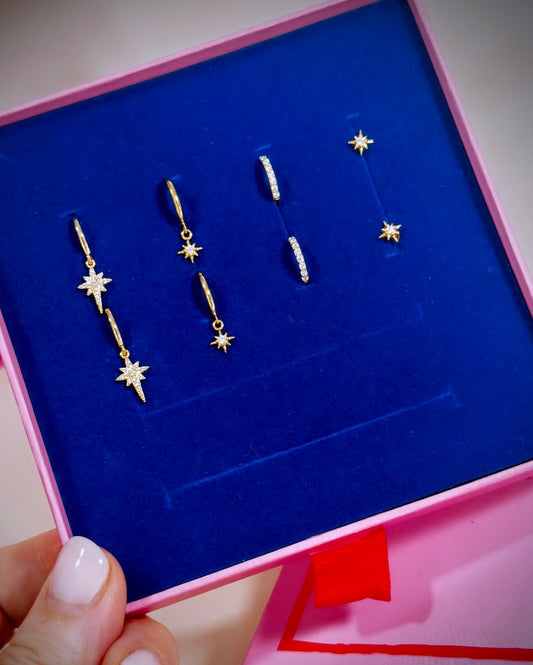 A collection of earrings including 1 set of north star drops, a smaller star drop, pave gold cz hoops and pair of star stud earring displayed in a giftbox.