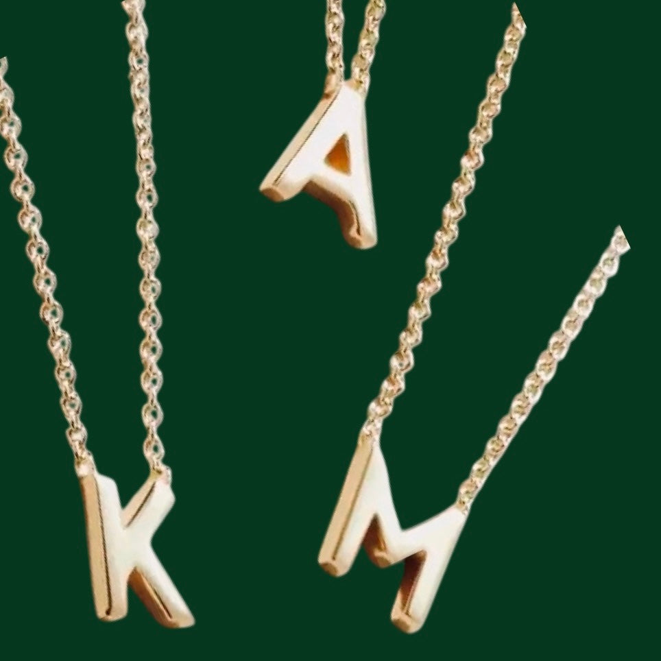 Gold necklaces with letter pendants on a green background