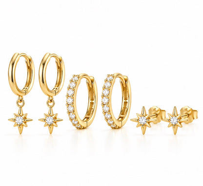 A set of gold huggie hoop earrings and stud earrings, featuring some hoops with clear pavé stones and others with dangling gold starburst charms set with round clear stones, displayed on a clean white background.