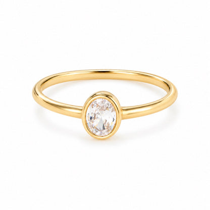 A delicate yellow gold ring featuring a bezel-set oval clear gemstone, shown on a clean white background.
