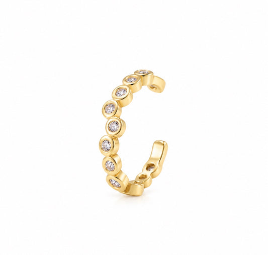 A gold ear cuff adorned with a row of bezel-set clear round stones, shown on a clean white background.