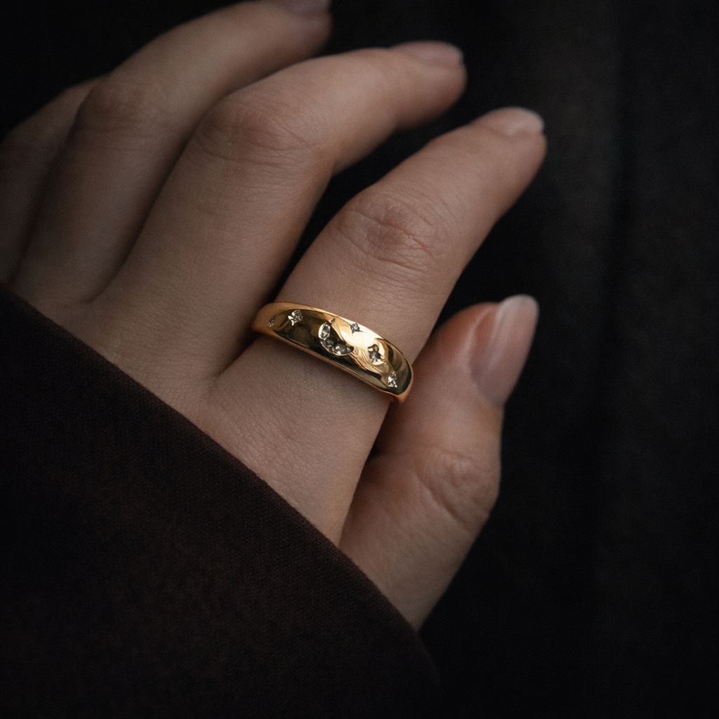 Gold ring with small stones on a person's finger against a dark background