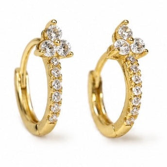 A pair of gold huggie hoop earrings decorated with clear cubic zirconia stones, featuring a trio cluster at the top and a line of small stones along the front, set against a plain white background.