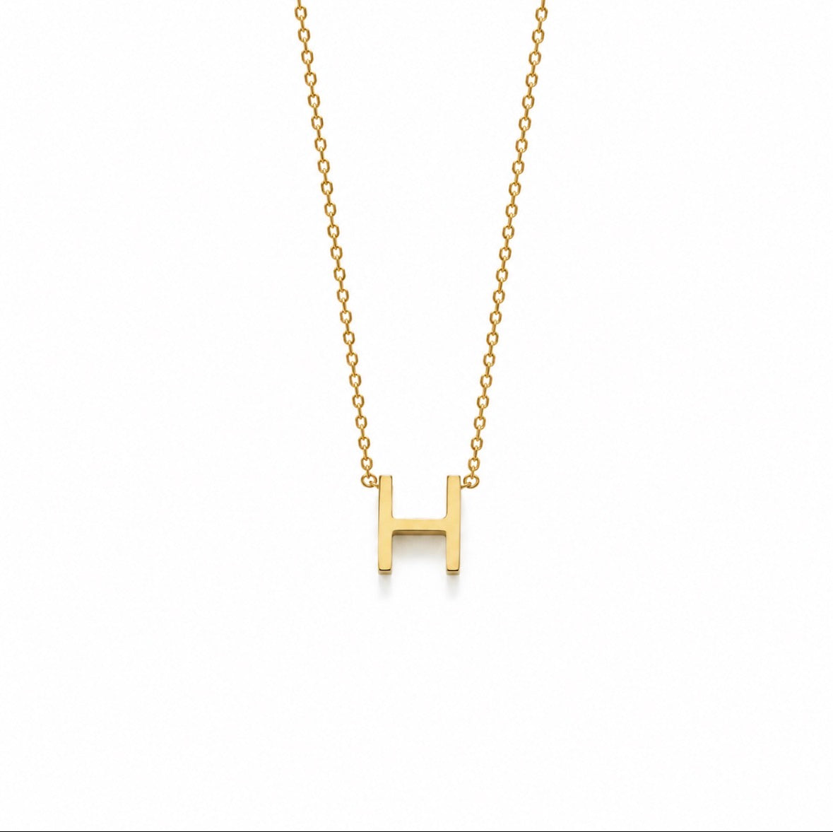 A gold initial necklace featuring a polished letter 'H' pendant on a delicate gold cable chain, shown against a plain white background.