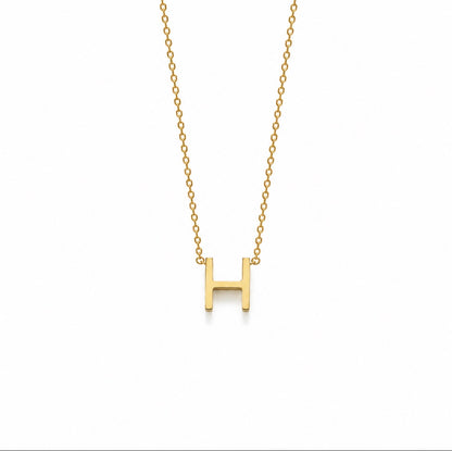 A gold initial necklace featuring a polished letter 'H' pendant on a delicate gold cable chain, shown against a plain white background.