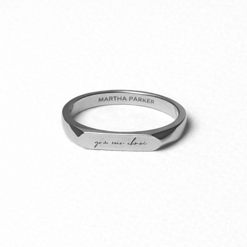 flat lay photo silver stainless steel ring with a light engaved irish phrase grá mo chorí meaning love of my heart. branding name martha parker on inside band