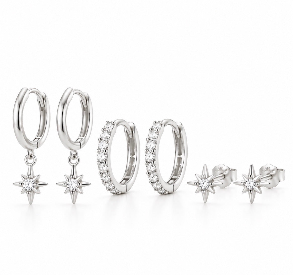A jewelry set featuring four silver-toned huggie hoop earrings and matching starburst stud earrings, all adorned with clear pavé and round stones, arranged on a clean white background.