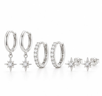 A jewelry set featuring four silver-toned huggie hoop earrings and matching starburst stud earrings, all adorned with clear pavé and round stones, arranged on a clean white background.