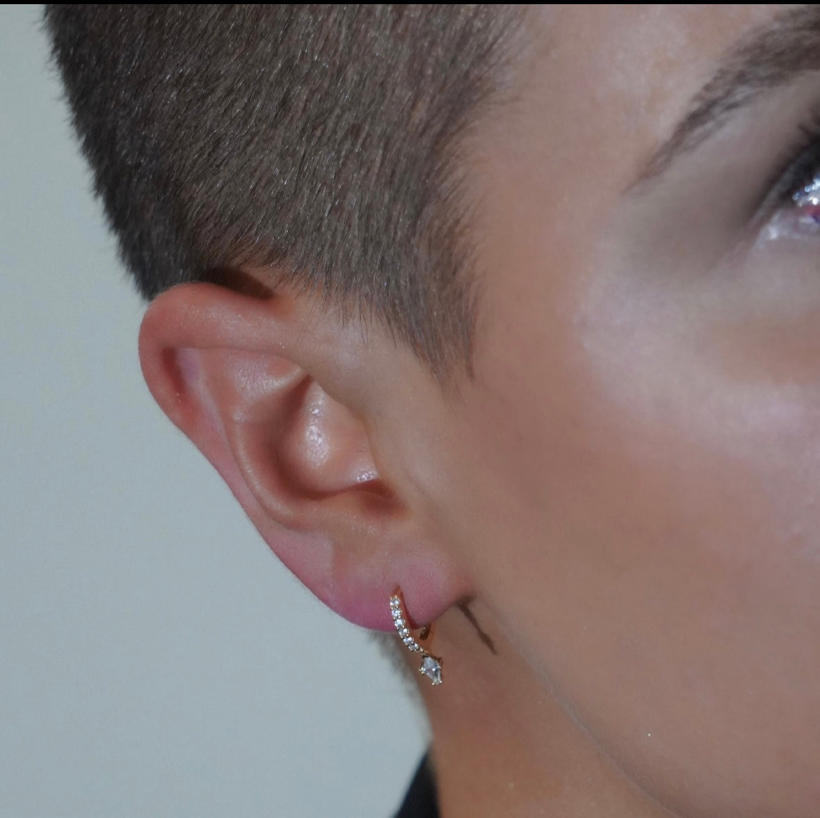 Close-up of an ear wearing Paloma cubic zirconia drop huggie hoop earring with a blurred background