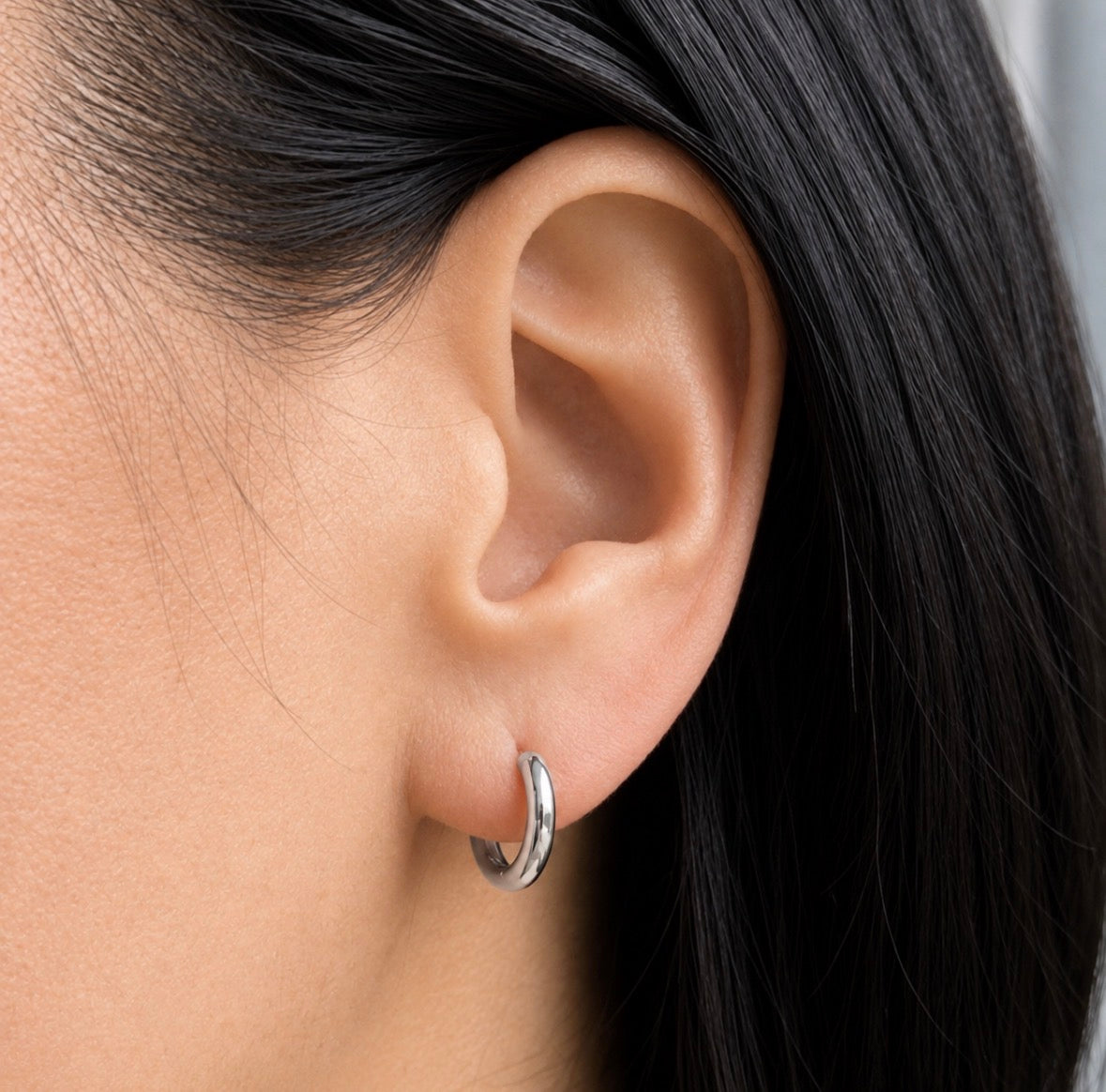 A close-up of a person's ear wearing a small silver hoop earring.