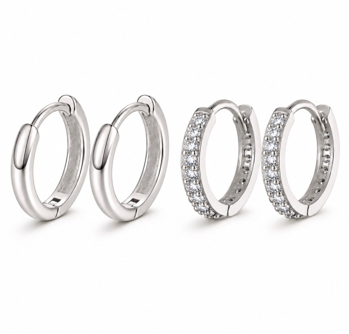 Four silver huggie hoop earrings on a white background, including two plain polished hoops and two pavé-set with clear stones.