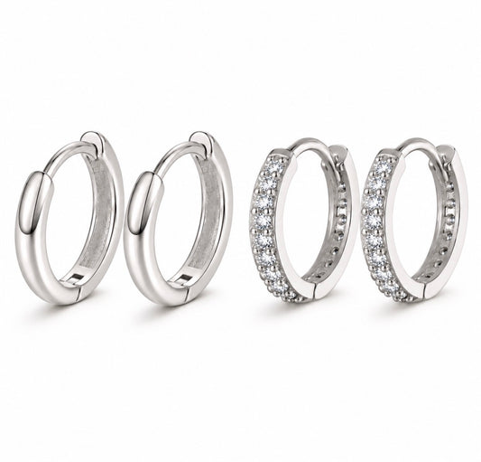 Four silver huggie hoop earrings on a white background, including two plain polished hoops and two pavé-set with clear stones.