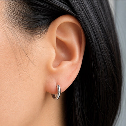 A close-up of a person's ear wearing a small polished silver hoop earring.