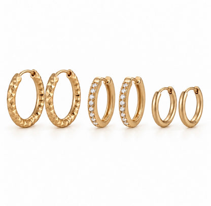 three pairs of gold huggie hoop earrings in different sizes, displayed on a clean white background. The earrings feature various textures and settings, including a textured diamond-cut finish, a pavé-set row of clear stones, and smooth polished finishes.