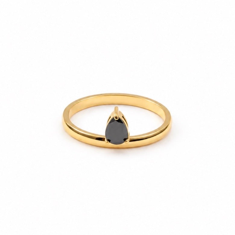 A gold ring featuring a single teardrop-shaped dark gray gemstone in a prong setting, shown against a plain white background.