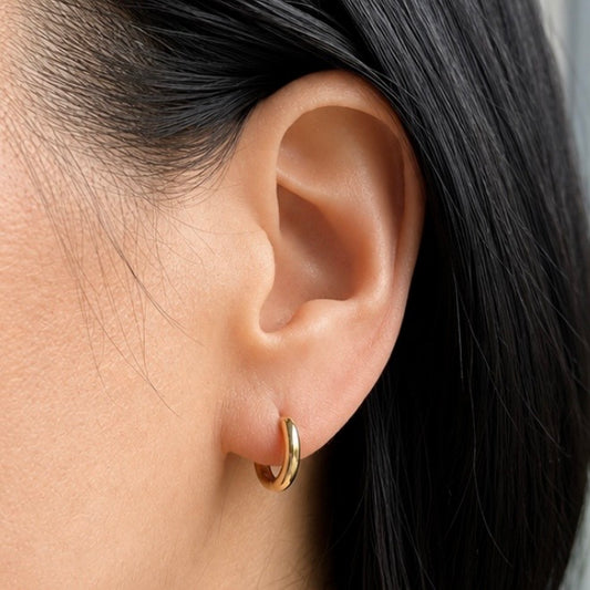 A close-up of a person's ear wearing a small gold hoop earring, with dark hair visible on the side.