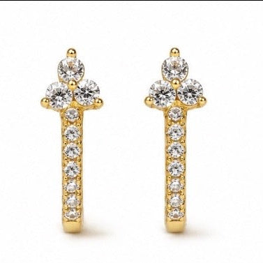 A pair of gold huggie hoop earrings decorated with clear round-cut gemstones, shown against a plain white background.