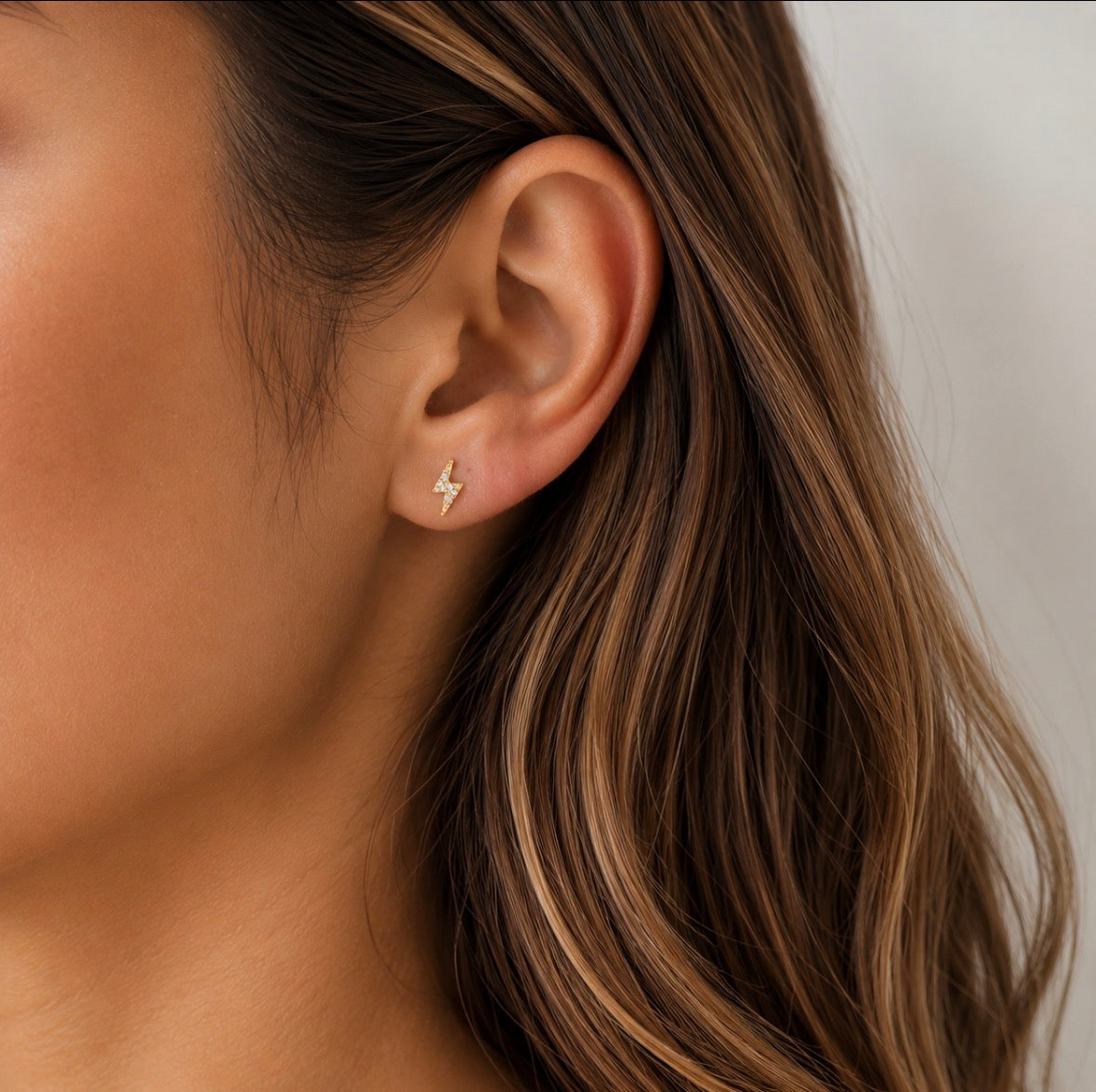 Close-up of an ear wearing a gold Lightning bolt shaped stud earring with a neutral background