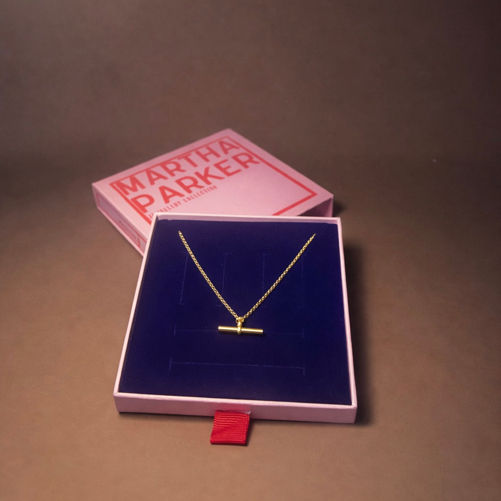 Gold necklace in a Martha Parker jewelry box on a brown surface