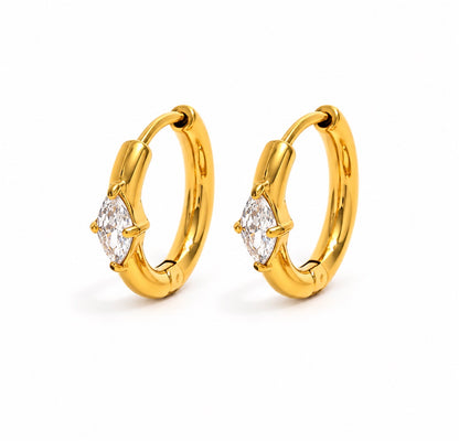 A pair of gold huggie hoop earrings, each featuring a marquise-cut clear gemstone in a prong setting, shown on a clean white background.