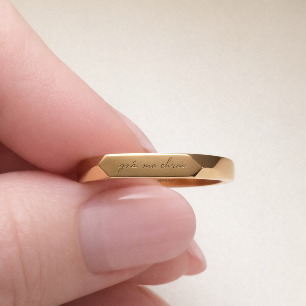 close up gold stainless steel ring with a light engraved Irish phrase grá mo chroí meaning love of my heart