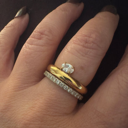 Close-up of a hand wearing two gold rings with diamond accents on a dark background