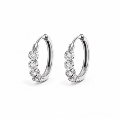 A pair of silver hoop earrings, each adorned with four round-cut clear gemstones in bezel settings, displayed on a clean white background.