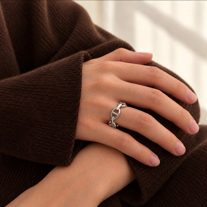 A close-up of a person's hand wearing a silver ring with a interlocking anchor link design, resting on a brown ribbed knit sweater.