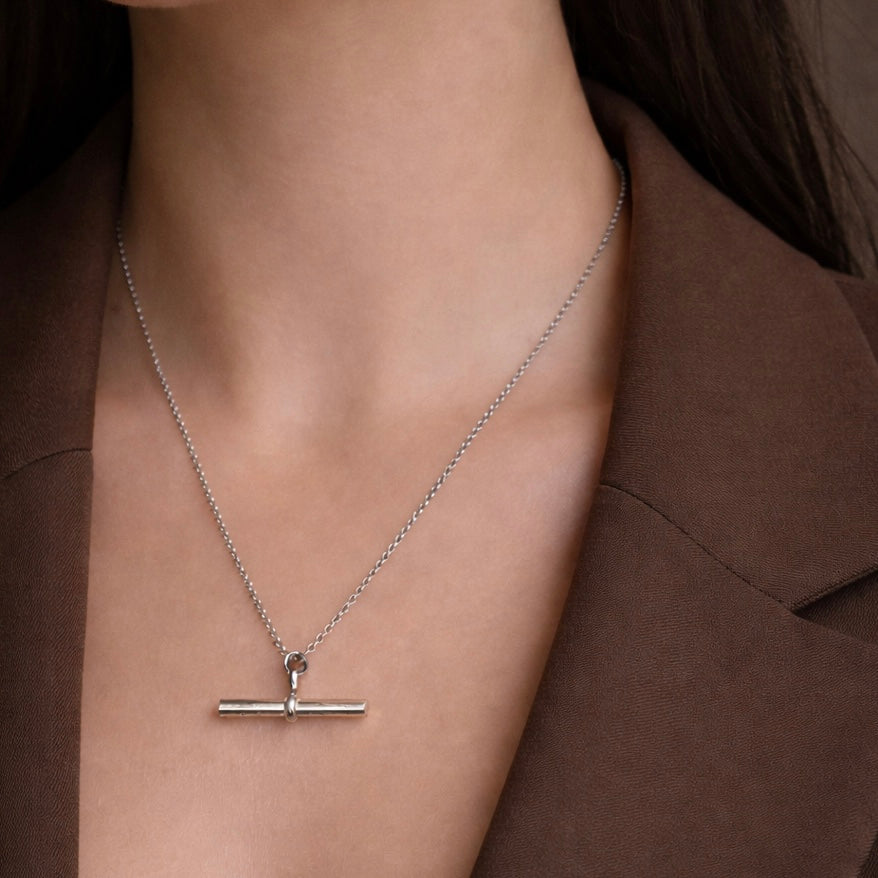 Silver necklace with a bar pendant worn by a person against a brown background