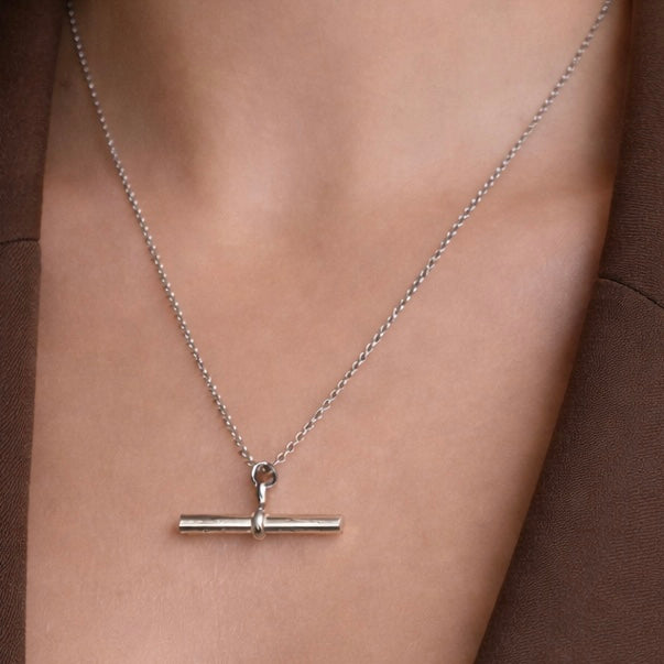 Silver necklace with a bar pendant on a person wearing a brown garment.