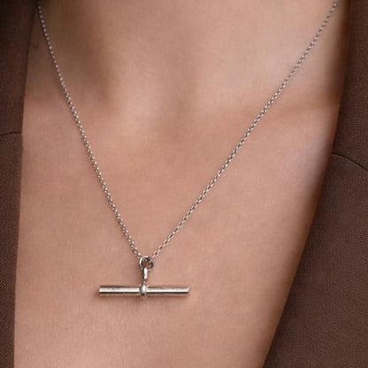 Silver necklace with a bar pendant on a person wearing a brown garment.