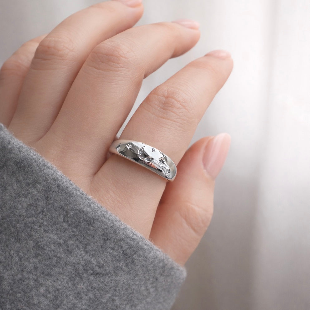 Silver dome ring with pave stars and crescent moon egraved with pave stones on a finger with a blurred background