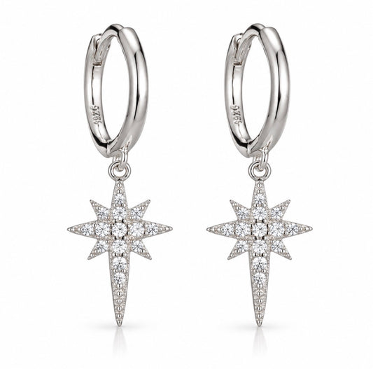 A pair of silver huggie hoop earrings with dangling starburst charms paved with clear stones, shown on a clean white background.