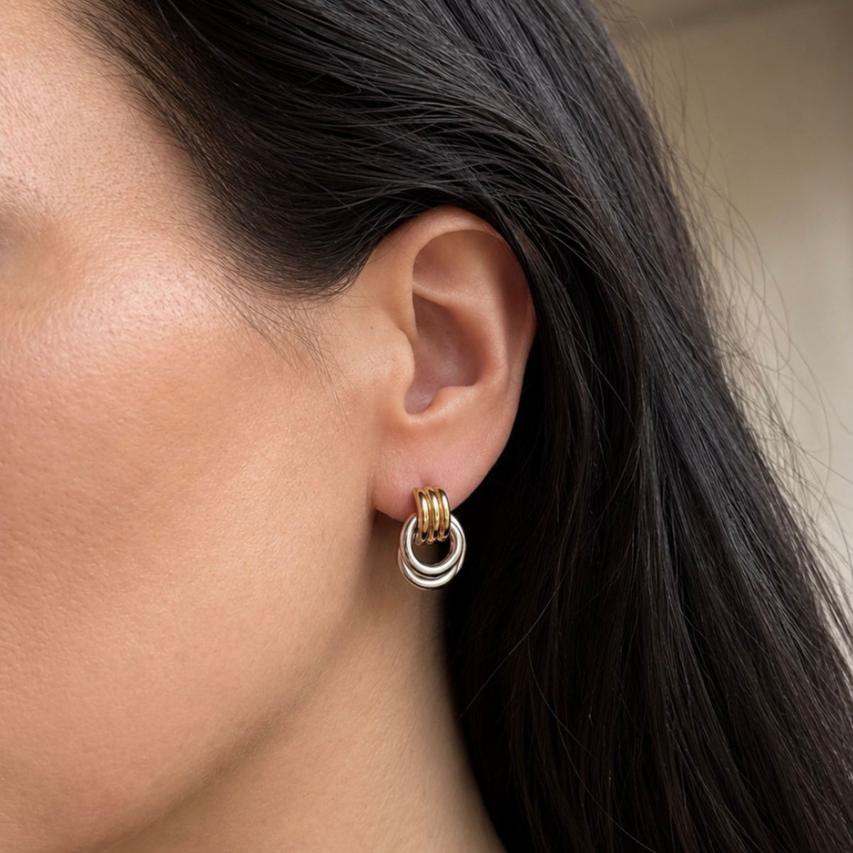 A close-up of a person's ear wearing a small hoop earring with a gold-toned top band and two stacked silver-tone hoops.